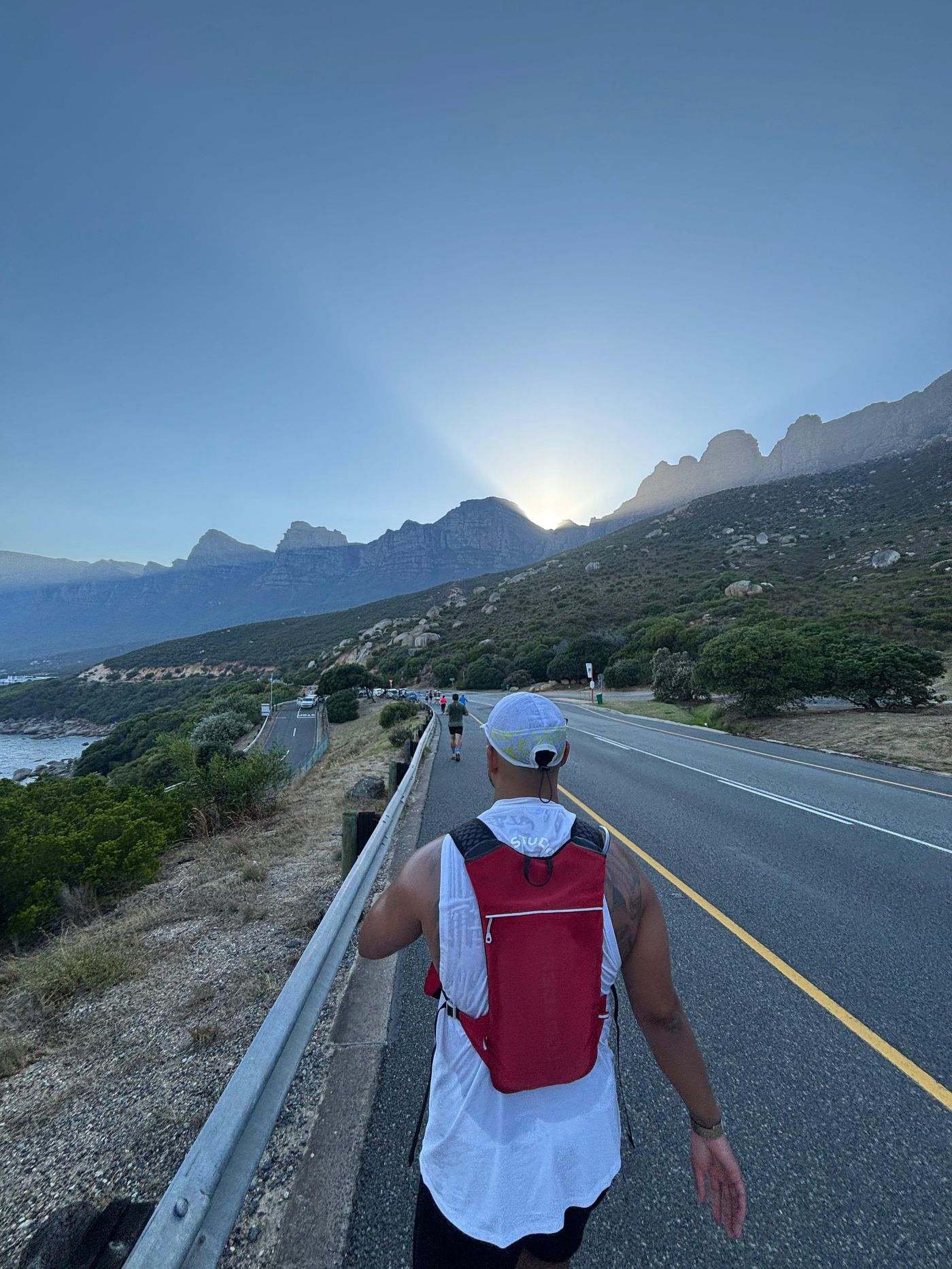 Shaun Cedric Thomas running on the coastal road at sunrise with mountains in the background, Cape Town